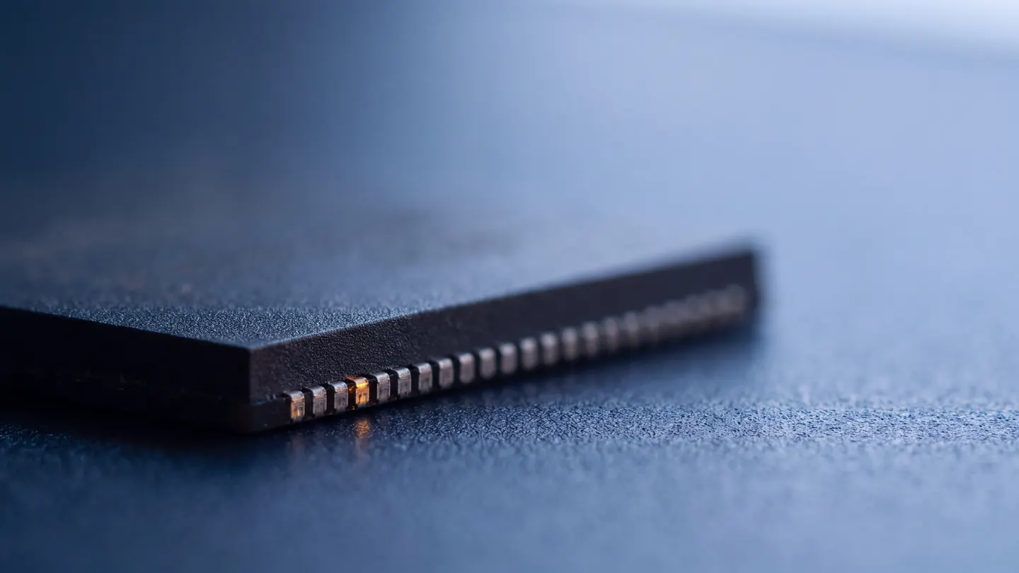 The edge of a microchip on deep blue, one contact catching the light